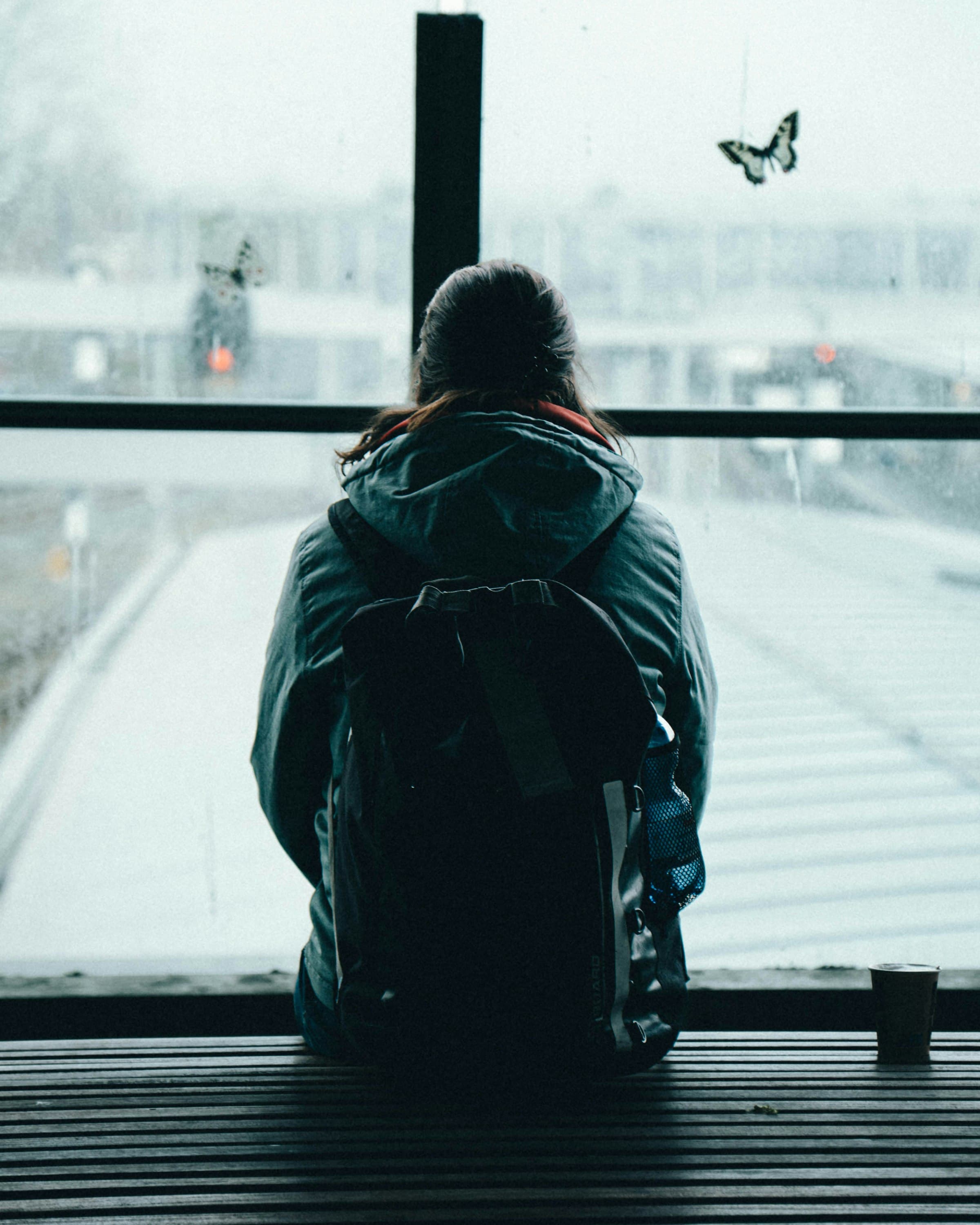 Person mit Rucksack sitzt auf einer Bank und schaut aus dem Fenster